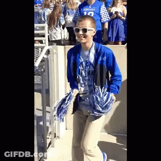 A Person Wearing Sunglasses And A Kentucky Shirt Is Holding Pom Poms While Walking . GIF