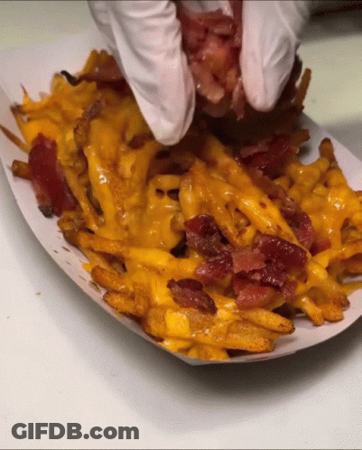 A Person Wearing White Gloves Holds A Piece Of Bacon Over French Fries GIF