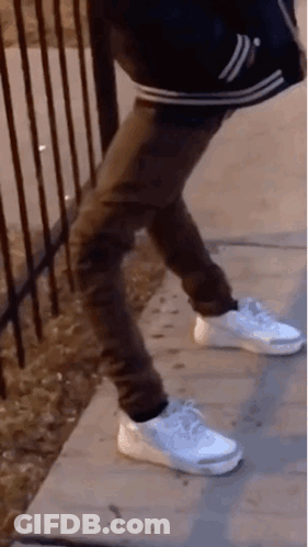 A Person Wearing White Nike Shoes Is Standing On A Sidewalk . GIF