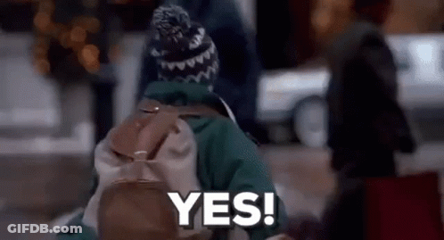 A Person With A Backpack And A Hat Is Walking Down The Street And Saying Yes . GIF