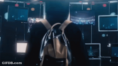 A Person With A Backpack Stands In Front Of A Wall With Monitors GIF