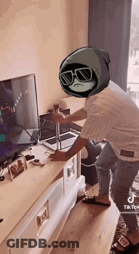 A Person With A Cartoon Character On Their Head Is Standing In Front Of A Laptop And A Television . GIF
