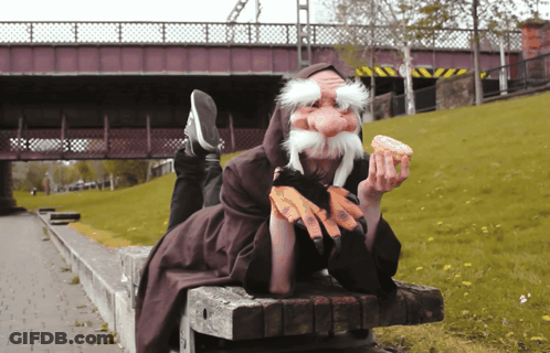 A Person With A Fake Beard Is Eating A Donut On A Bench GIF