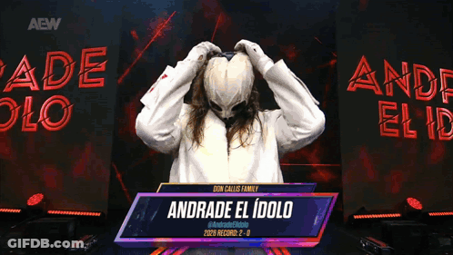 A Person With A Mask On Stands In Front Of A Sign That Reads Andrade El Idolo GIF