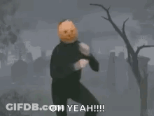A Person With A Pumpkin On Their Head Is Standing On One Leg In A Cemetery . GIF