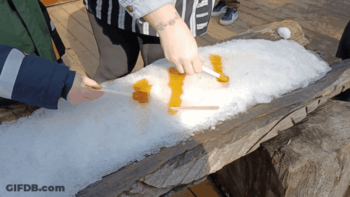 A Person With A Tattoo On Their Arm Is Spreading Maple Syrup On A Pile Of Snow GIF