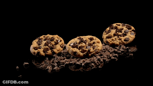 A Person With Black Nails Is Holding A Chocolate Chip Cookie In Their Hands GIF