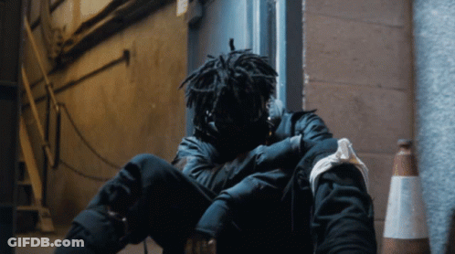 A Person With Dreadlocks Is Sitting On The Ground With Their Head Down GIF
