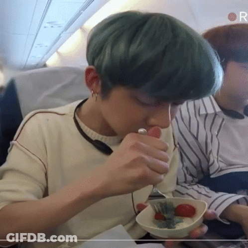 A Person With Green Hair Is Eating A Bowl Of Food On An Airplane GIF