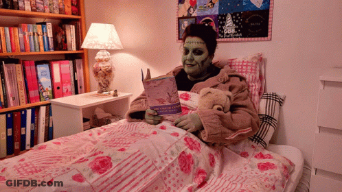 A Person With Green Paint On Their Face Is Reading A Book In A Bed With A Teddy Bear GIF