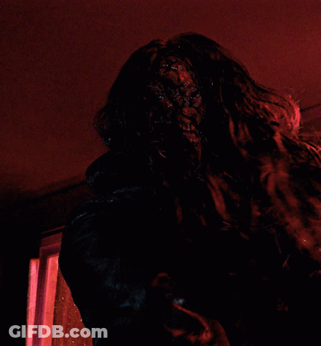 A Person With Long Hair Is Standing In A Dark Room With A Red Light Behind Them GIF