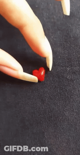 A Person With Long Nails Is Holding A Small Red Heart In Their Hand GIF