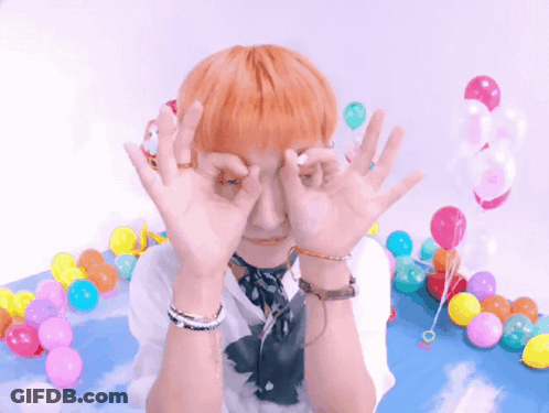 A Person With Orange Hair Covering Their Eyes With Their Hands In Front Of Balloons GIF