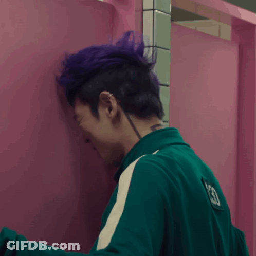 A Person With Purple Hair Leaning Against A Pink Wall GIF