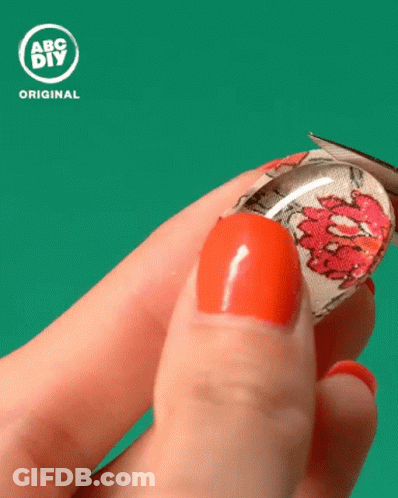 A Person With Red Nails Is Holding A Glass Cabochon With A Floral Design On It In Front Of An Abc DIY Original Logo GIF