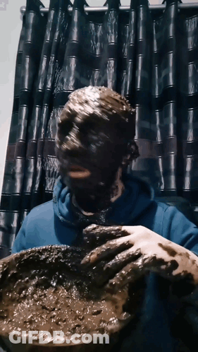 A Person With Their Face Covered In Mud Holds A Bowl GIF