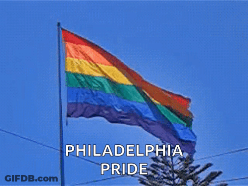 A Philadelphia Pride Flag Is Flying In The Wind Against A Blue Sky GIF