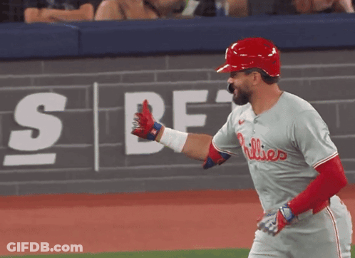 A Phillies Baseball Player Is Giving A High Five In Front Of A Wall That Says Sbf GIF