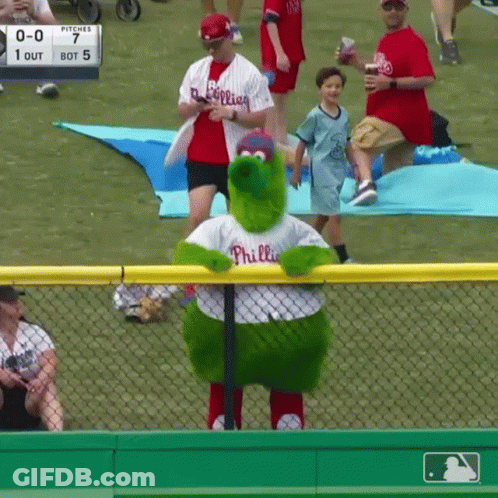 A Phillies Mascot Stands In Front Of A Fence At A Baseball Game GIF