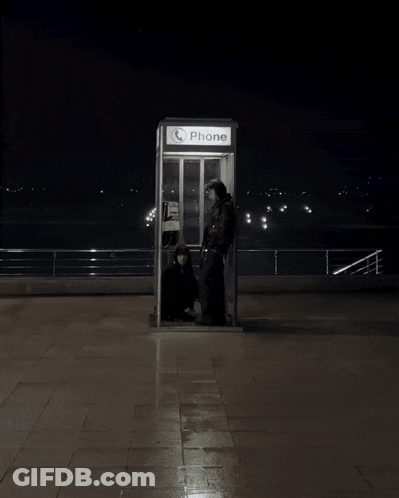 A Phone Booth Is Lit Up At Night With Two People Inside GIF