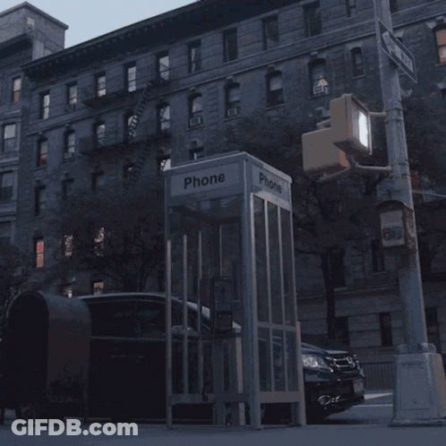 A Phone Booth Sits On The Side Of A Street GIF