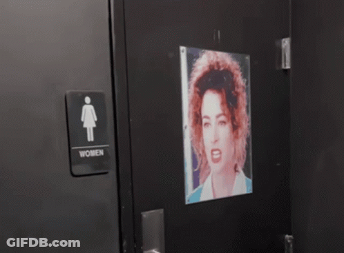 A Picture Of A Man With A Mustache Is Projected On A Wall Next To A Sign For A Men 'S Restroom GIF