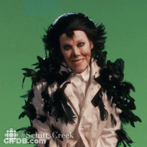 A Picture Of A Woman With Black Feathers Around Her Neck And The Words Schitts Creek GIF