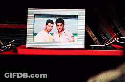 A Picture Of Two Men In A Frame Is On A Red Shelf GIF