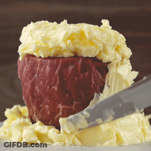 A Piece Of Meat Is Covered In Butter And Being Sliced By A Knife GIF