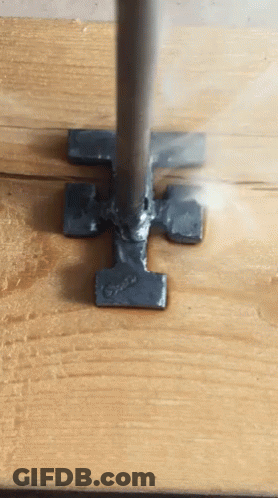 A Piece Of Metal That Looks Like A Hammer Is On A Wooden Surface GIF