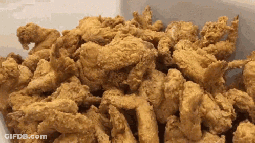 A Pile Of Fried Chicken Is Sitting On A White Surface . GIF