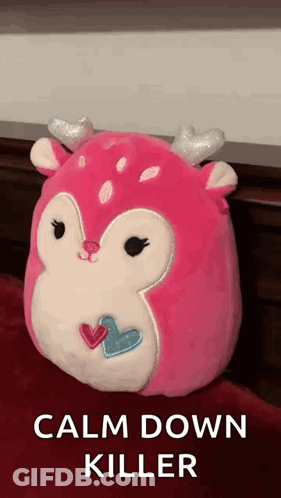 A Pink Deer Stuffed Animal With Hearts On Its Face Is Sitting On A Bed . GIF