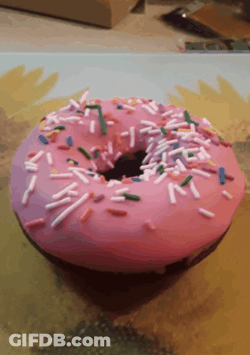 A Pink Donut With Sprinkles And A Hole In It GIF
