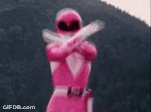 A Pink Power Ranger Is Standing In Front Of A Mountain Holding Two Guns . GIF