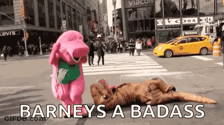 A Pink Stuffed Animal Is Standing Next To A Person In A Dinosaur Costume On A Street . GIF