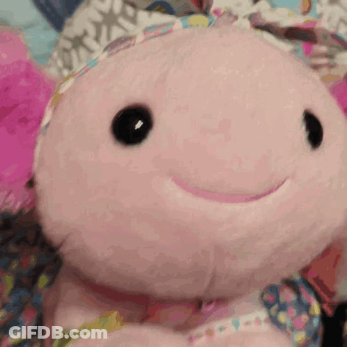 A Pink Stuffed Animal With Black Eyes And A Smile On Its Face GIF