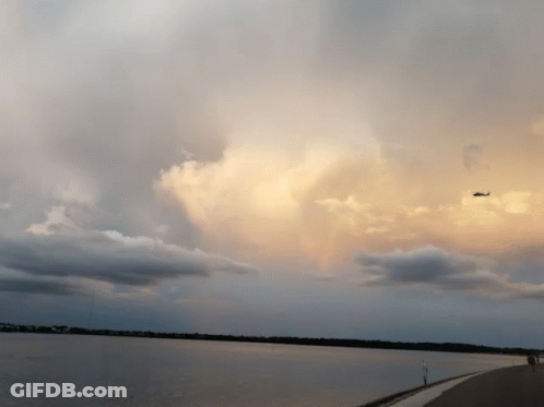 A Plane Is Flying Over A Body Of Water With Clouds In The Sky GIF