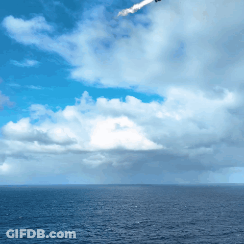 A Plane Is Flying Over The Ocean With A Blue Sky And White Clouds GIF