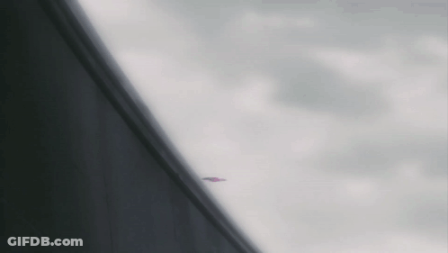 A Plane Is Flying Through A Cloudy Sky Behind A Building GIF