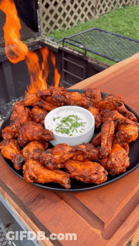 A Plate Of Chicken Wings With A Dipping Sauce On A Wooden Table GIF