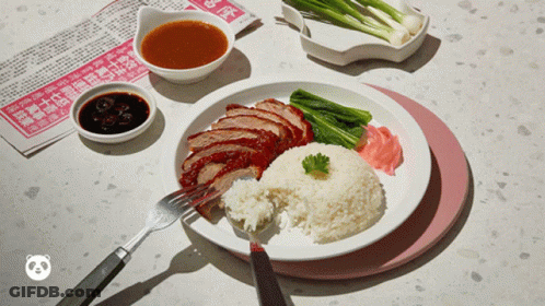 A Plate Of Food With Rice And Meat On A Table With A Newspaper In The Background GIF