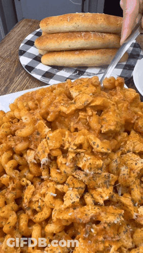 A Plate Of Macaroni And Cheese With Garlic Bread On A Table GIF