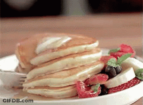 A Plate Of Pancakes With Strawberries , Bananas , Blueberries And Syrup On A Table . GIF