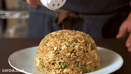 A Plate Of Rice And Vegetables With A Person Pouring Salt On Top GIF