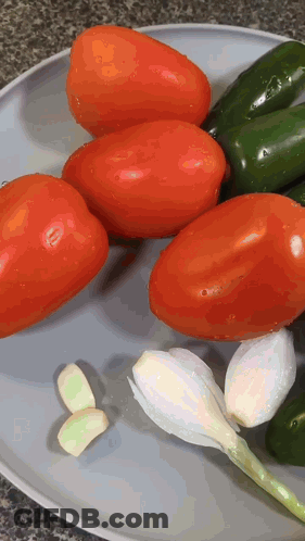 A Plate Of Tomatoes Peppers And Garlic On A Counter Top GIF