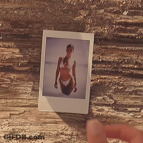 A Polaroid Picture Of A Woman In A Bikini On A Wooden Table GIF