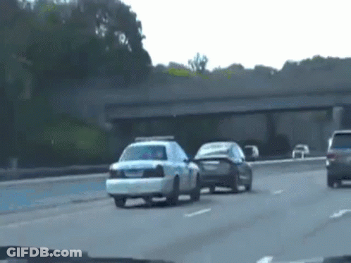 A Police Car Is Driving Down A Highway Next To A Black Car . GIF