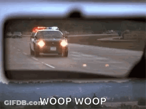 A Police Car Is Driving Down The Road In The Rear View Mirror Of A Car . GIF