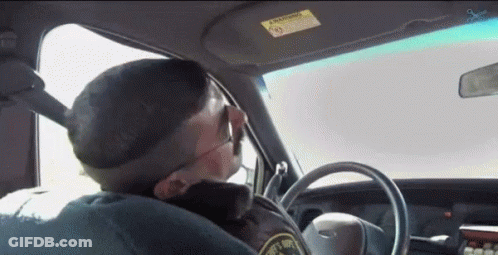 A Police Officer Is Driving A Car And Smoking A Cigarette While Wearing Sunglasses . GIF
