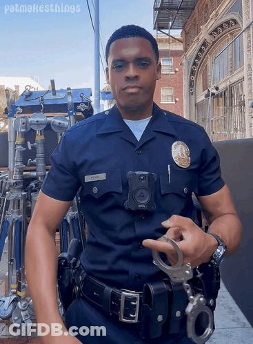 A Police Officer Is Holding A Pair Of Handcuffs In Front Of A Building With Patmakesthings Written Below Him GIF